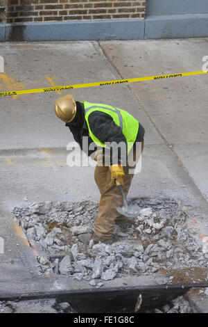 Operaio edile rimuovere manualmente il calcestruzzo rotto i detriti da un foro del marciapiede con una pala (FE1G87, Fe1G84, Fe1G8A) Foto Stock