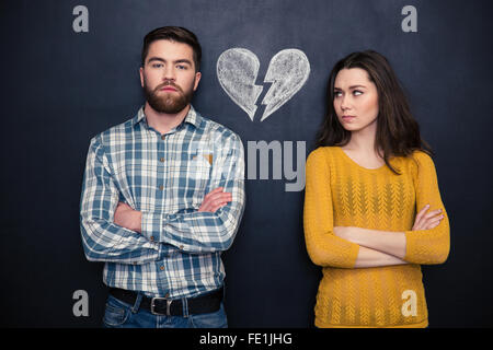 Ritratto di giovane coppia dopo l'argomento separatamente in piedi con le mani ripiegate su sfondo blackboard Foto Stock