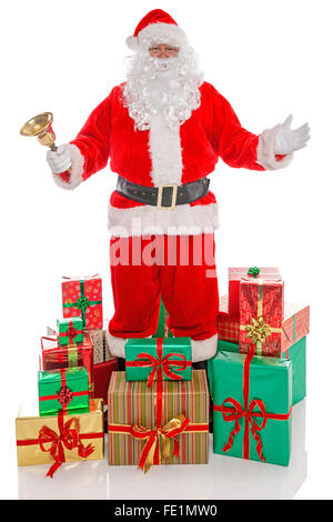 Babbo Natale tenendo un campanello d'oro circondato da pile di regalo presenta, isolato su sfondo bianco Foto Stock