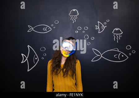 Piuttosto giovane donna in maschera subacquea e snorkeling in posa su lavagna con sfondo disegnato il mondo sottomarino Foto Stock