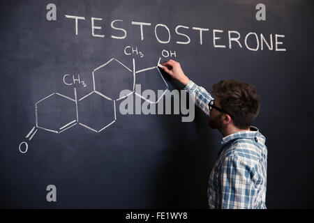 Concentrato giovane studente in bicchieri di Disegno struttura chimica della molecola di testosterone sulla lavagna Foto Stock