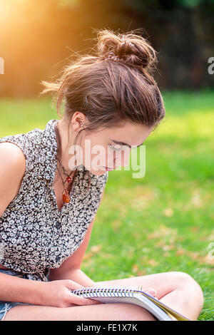 Ragazza adolescente è seduta su un prato e la scrittura Foto Stock