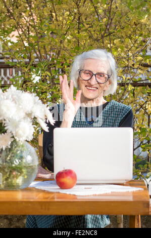 90 anni donna sventolare mentre avente una chiamata video su un notebook bianco Foto Stock