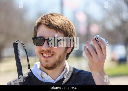 Ragazzo cieco con canna utilizzando la tecnologia assistiva nel suo quartiere Foto Stock