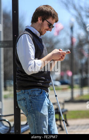 Ragazzo cieco in corrispondenza di una fermata bus utilizzando la tecnologia assistiva Foto Stock