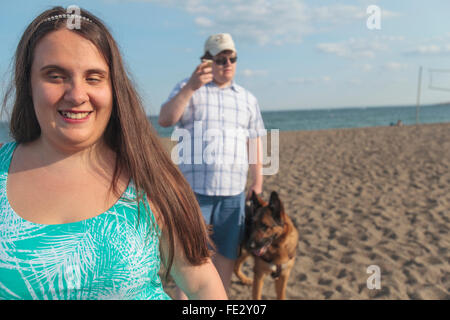 Cieco matura camminando lungo la spiaggia con il suo cane di servizio mentre si utilizza la sua tecnologia assistiva Foto Stock