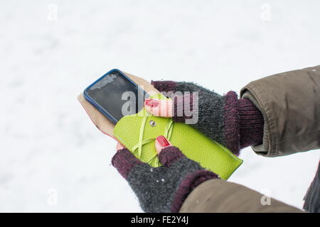 Mani femminili in guanti tenendo uno smartphone Foto Stock