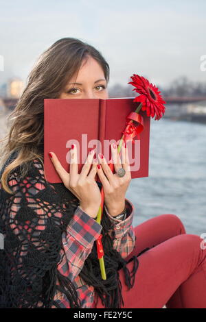 Bella bruna ragazza con un libro dal fiume bank holding fiore rosso Foto Stock