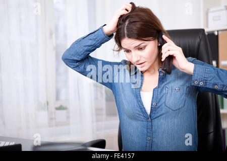 Frustrati preoccupato imprenditrice seduto alla sua scrivania parlando al telefono e graffiare la sua testa Foto Stock