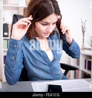 Preoccupato imprenditrice di prendere una chiamata telefonica accigliata come ascolta la conversazione mentre si sta guardando un rapporto steso su di lui Foto Stock