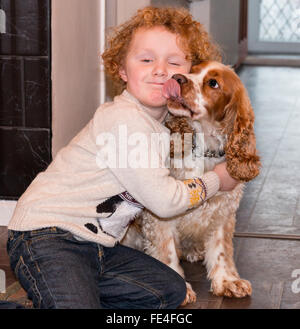 Un felice ragazzo sorridente con i capelli ricci rossi abbraccia il suo cane gattino spaniel Foto Stock