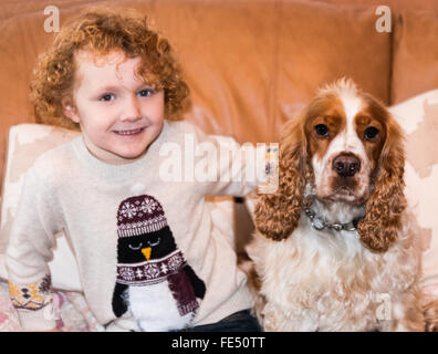 Un felice ragazzo sorridente con i capelli ricci rossi abbraccia il suo cane gattino spaniel Foto Stock