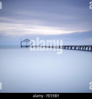 Il molo di legno o della banchina di silhouette in un oceano blu sul tramonto. Una lunga esposizione fotografie scattate in autunno in una spiaggia italiana Foto Stock