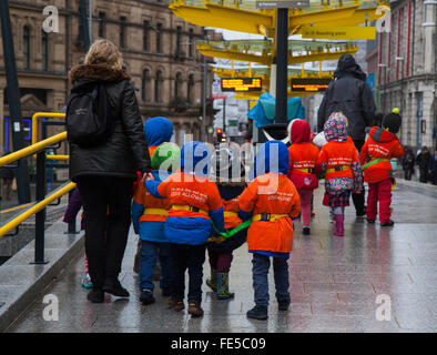 Bambini della scuola con reggetta e protezione. I bambini che camminano attraverso la strada indossando le giacche fluorescenti protettive di rischio di alta visibilità durante il Capodanno cinese, Manchester, Regno Unito. 4th Feb 2016. Gli allievi della scuola hanno collegato in una giornata fuori per vedere i preparativi per il capodanno cinese questo fine settimana. Foto Stock