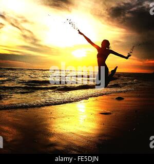 Donna salta sulla spiaggia di sabbia durante il tramonto
