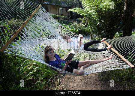 Ragazzo e una ragazza di lettura su un enorme amaca a Punga Cove, Queen Charlotte Track, Marlborough, Nuova Zelanda Foto Stock