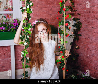 Cute girl teen in bicchieri siede su un altalena. Altalena decorata con fiori. Foto Stock