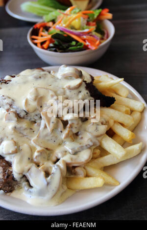 Una piastra di bistecca e patatine con una ciotola di insalata greca in background Foto Stock