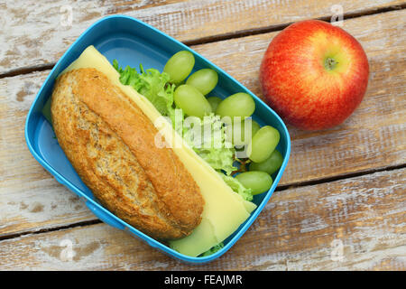 Pranzo sano scatola contenente il pane marrone sandwich di formaggio, uva e mela rossa Foto Stock