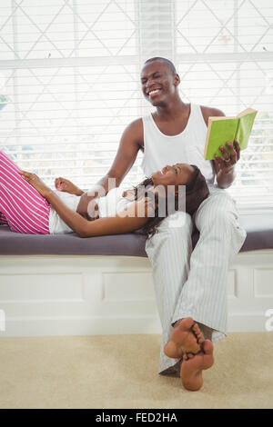 Donna in appoggio sulle gambe oh il suo fidanzato la lettura di un libro Foto Stock