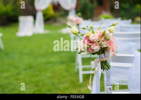 Sedia bianca in piedi su un green glade, preparato per la cerimonia di nozze. La sedia è decorata con un bouquet di fiori. Il Foto Stock