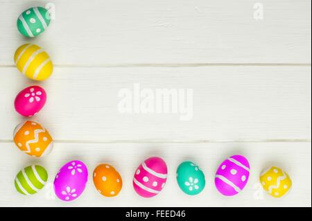 Coloratissimo uovo di pasqua angolo bordo contro un bianco sullo sfondo di legno Foto Stock