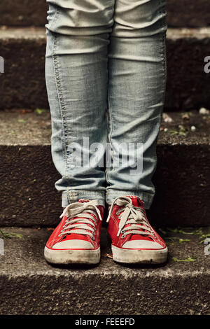 Bambina in rosso sneakers e jeans in piedi su per le scale. Facendo prima fase. Foto Stock