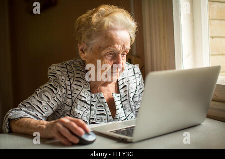 Donna anziana lavorando sul portatile a casa seduti a tavola. Foto Stock