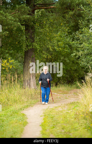 Una donna anziana in una passeggiata nel parco la pratica del Nordic walking. Foto Stock