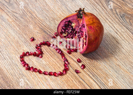Il Melograno e i suoi semi stabiliti a forma di cuore su una texture di legno Foto Stock
