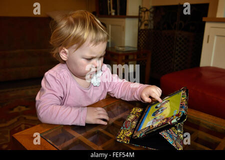 Un diciotto mesi concentrando toddler durante la riproduzione di un gioco su un ipad nella sua casa. Foto Stock