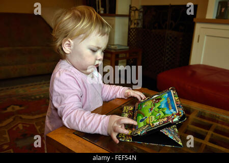 Un diciotto mesi concentrando toddler durante la riproduzione di un gioco su un ipad nella sua casa. Foto Stock