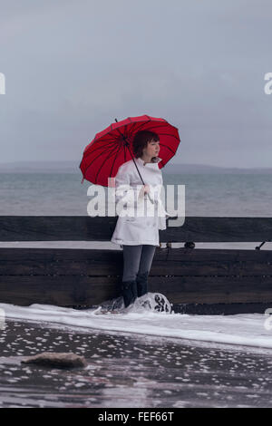 Una donna in camice bianco con un ombrello Rosso al mare in inverno Foto Stock