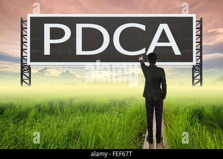 Business man in piedi sul ponte di legno tra il campo di riso e dispositivo di puntamento con grande segno di PDCA (concetto aziendale) Foto Stock