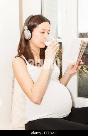 Donne in stato di gravidanza per bere un bicchiere di latte e ascolto di musica Foto Stock