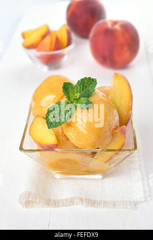 Peach gelato nel contenitore in vetro e frutta fresca Foto Stock