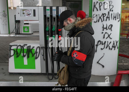 Kiev, Ucraina. 06 feb 2016. Un uomo con il volto coperto e con simboli nazionalistici sul suo braccio passa da uno slogan "sangue di ucraini sulle loro mani' scritto su le costrizioni di AMIC stazione di rifornimento di Kyiv. Ukrainian lontano i diritti di chiamata per il boicottaggio delle banche russe e stazioni di riempimento reti in Ucraina. © Sergii Kharchenko/Pacific Press/Alamy Live News Foto Stock