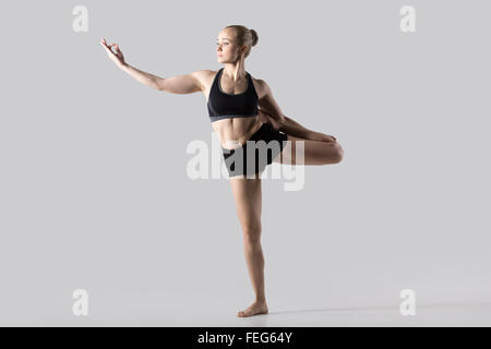 Sporty bella giovane donna a praticare yoga, facendo la variazione di Natarajasana, Signore della danza o Re Posizione del signore della danza Foto Stock