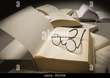 Coppia di occhiali da lettura sulla parte superiore di un libro aperto, vicino ad altri libri aperti Foto Stock