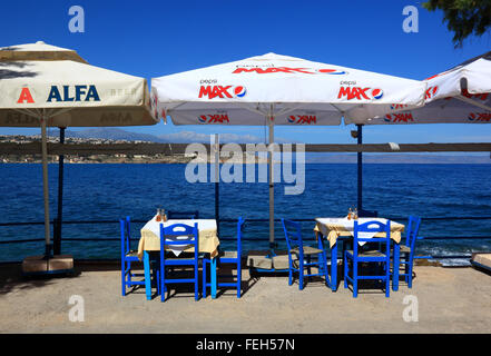 Creta, Rethymnon, street restaurant con sguardo sul mare blu, sedie, tavoli e ombrelloni Foto Stock