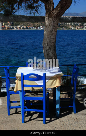 Creta, Rethymnon, street restaurant con sguardo sul mare blu, sedie, tavoli e ombrelloni Foto Stock