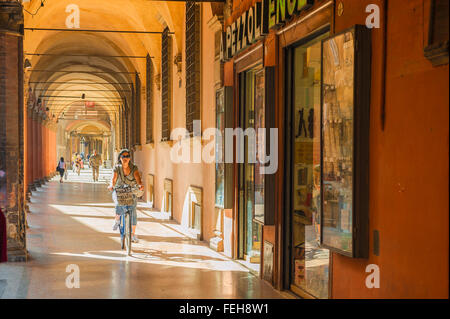 Bologna centro storico, vista in estate di una donna in bicicletta sotto un portico medievale in Strada Maggiore a Bologna città vecchia (Centro Storico), Italia. Foto Stock