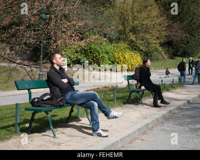 Persone in un parco sedersi sulle panchine di crogiolarvi al sole di calore Foto Stock