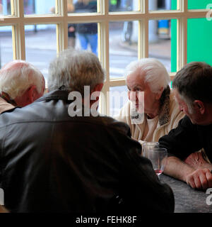 Una donna anziana si impegna in tre uomini, tutto proteso verso di lei in un ambiente intimo e accattivante conversazione in un ristorante tabella Foto Stock