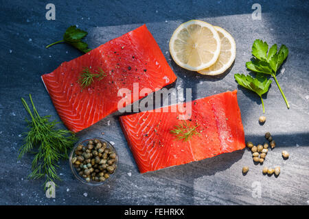 Due pezzi di materie di salmoni selvatici bistecca di pesce con il limone, i capperi e le erbe aromatiche, pronto a cucinare, dall'alto. Foto Stock