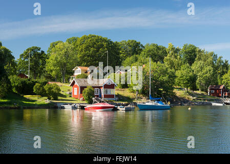 Bay con il tipico rosso svedese case, Barche e Yachts su Yxlan isola nell'arcipelago d'estate,Norrtälje,Svezia Foto Stock