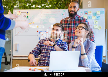 Gruppo Muliethnic di felice giovani seduti sul meeting di lavoro e di ascolto altoparlante Foto Stock