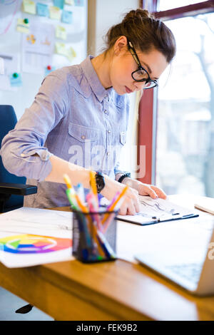 Focalizzato bella giovane donna fashion designer in bicchieri schizzi di disegno sul posto di lavoro Foto Stock