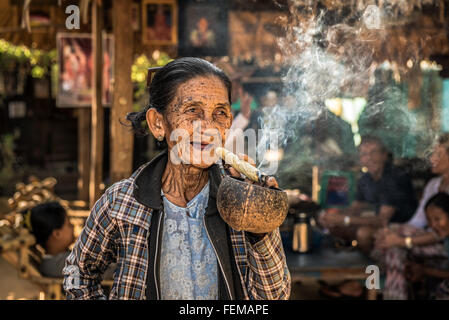 Felice e vecchia donna rugosa fuma una grande cheroot sigaro in pubblico Foto Stock
