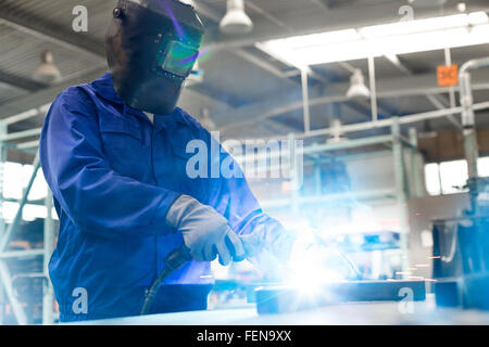 Saldatore in indumenti da lavoro di protezione utilizzando la torcia di saldatura in fabbrica di acciaio Foto Stock